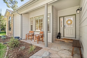 A house with a stone foundation, a front porch with two wooden chairs, a door with a wreath, and a stone-paved entrance. - Fairway & Fly at Sopris - Fishing, Golf, & Hot Tub (Carbondale)