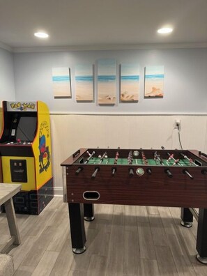 Ein Kicker steht in einem Raum mit Strandmotiven an der Wand und einer bunten Spielautomat.