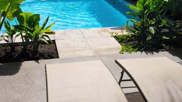 A swimming pool with lounge chairs and tropical plants.