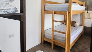 Una cama individual con estructura de madera y ropa de cama blanca, una ventana con vistas, y una alfombra mullida blanca en el suelo.