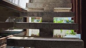 Una escalera de concreto lleva a un área de piscina con una valla de madera y palmeras al fondo.