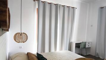 A bedroom with a bed, a desk, a chair, a hanging light fixture, and a ceiling fan.