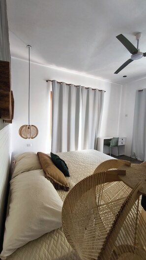 Une chambre à coucher comprenant un lit, un bureau, une chaise, un luminaire suspendu et un ventilateur de plafond.