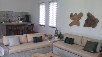 Uma sala de estar moderna com um sofá seccional, uma mesa de centro e uma área de refeições com cozinha ao fundo.