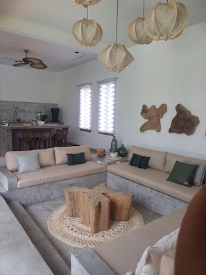 A modern living room with a sectional sofa, a coffee table, and a dining area with a kitchen in the background. - Areia Brisa A/CPiscina privada fam a pasos del mar (El Paredón Buena Vista)