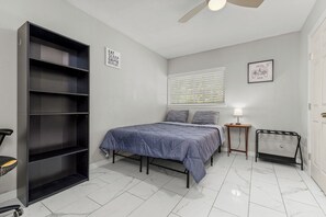 A bedroom with a bed, a wardrobe, a bedside table, a lamp, and a window with blinds.