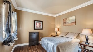 Um quarto com cama, mesas de cabeceira, cômoda e janela com cortinas.