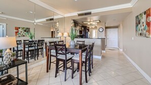 Uma ampla área de refeições com uma grande mesa de madeira e cadeiras, uma cozinha ao fundo, e um design de interiores moderno.