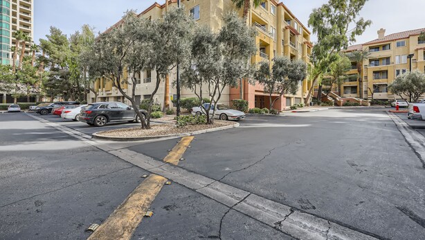 Um edifício residencial com várias andares e varandas, rodeado por árvores e carros estacionados.