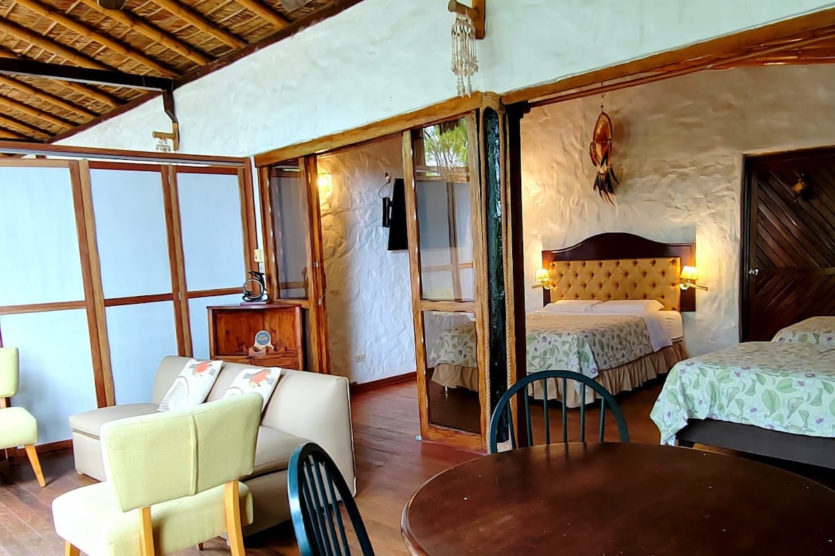 A room with a bed, a table, and a chair. There is a wooden ceiling and a wall with a textured pattern.