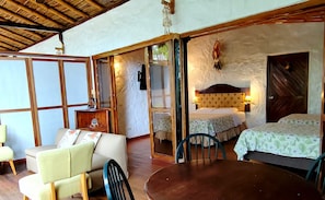 A room with a bed, a table, and a chair. There is a wooden ceiling and a wall with a textured pattern.