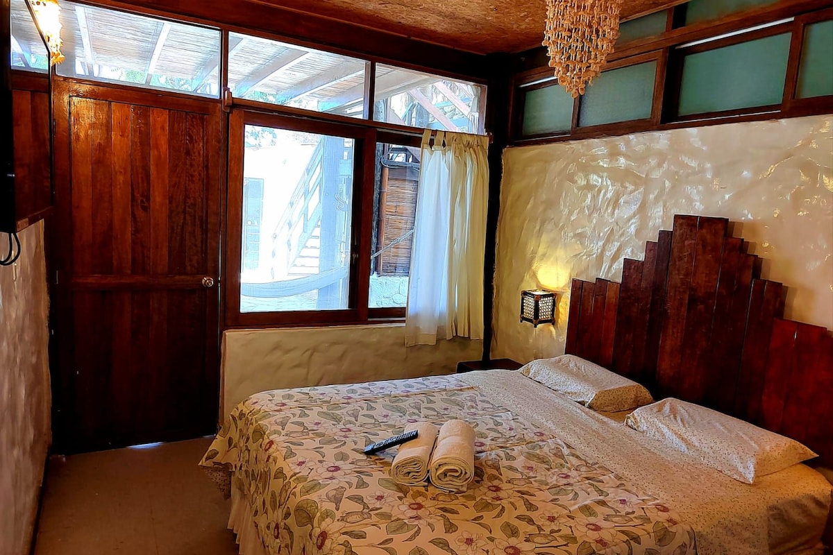 A bedroom with a large bed, wooden headboard, and a view of the outside through a window.
