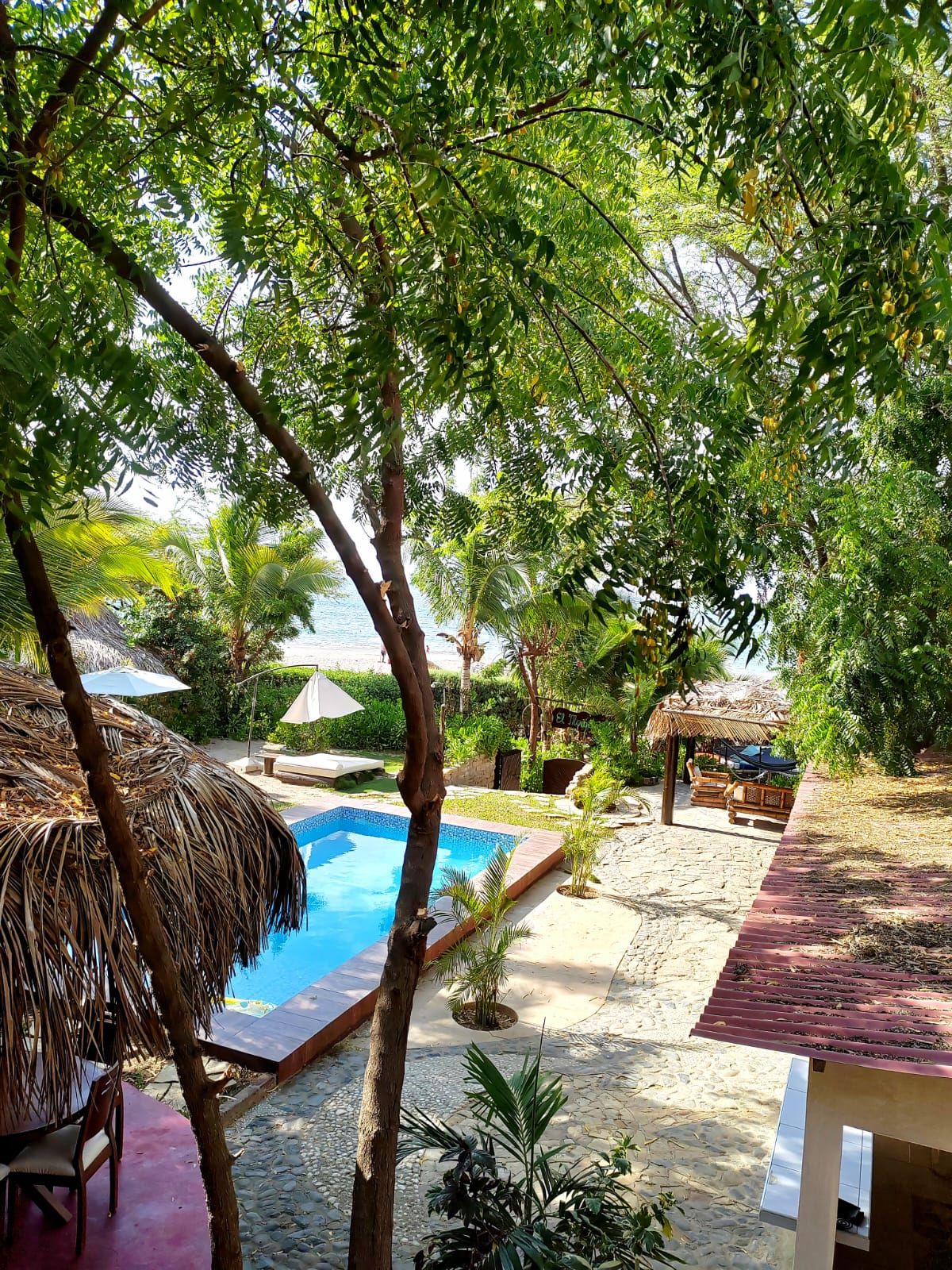 A pool area with a thatched umbrella, lounge chairs, and a view of the beach.