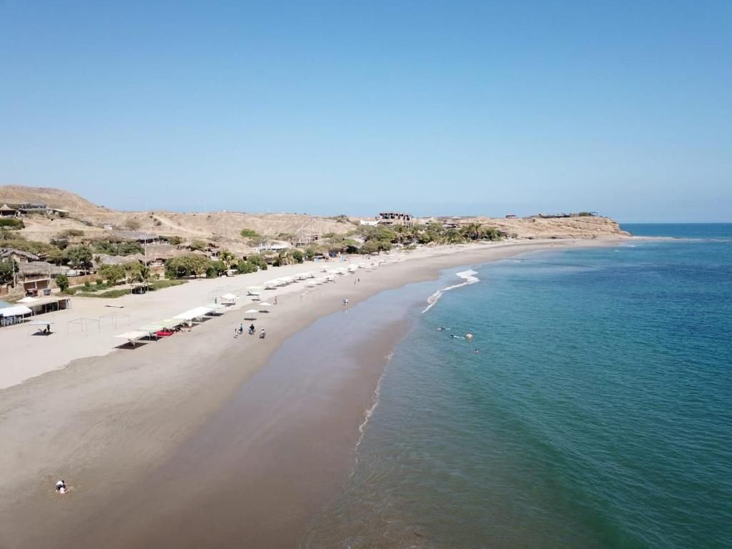 A coastal beach with a sandy shore, a few buildings, and a clear sky.