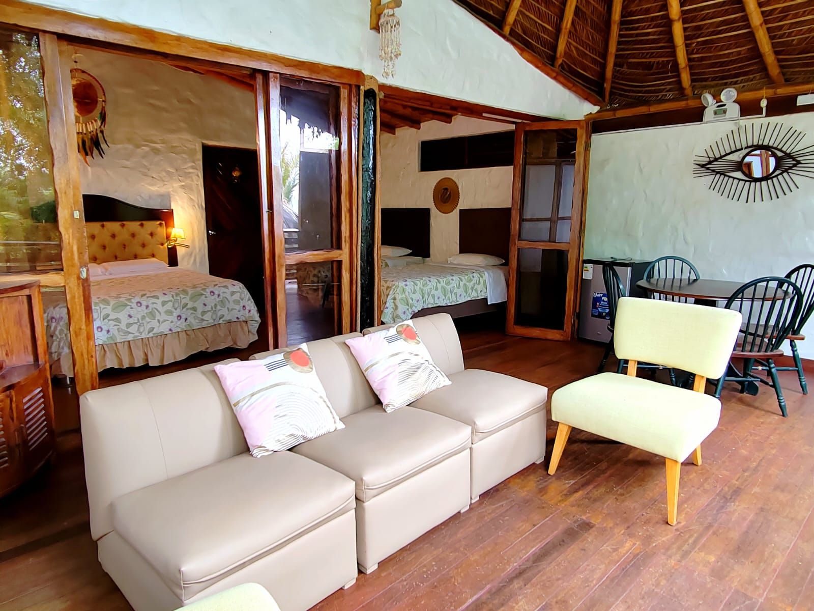 A room with a sofa, a dining table with chairs, a bed with a canopy, and a wall with a decorative eye design.