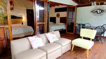 A room with a sofa, a dining table with chairs, a bed with a canopy, and a wall with a decorative eye design.