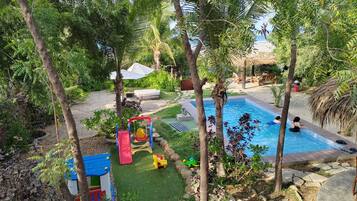 A backyard with a swimming pool, a children's play area, and a seating area with a view of the sea.