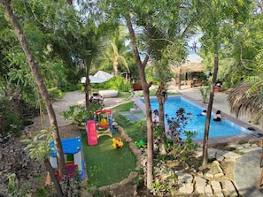 A backyard with a swimming pool, a children's play area, and a seating area with a view of the sea.