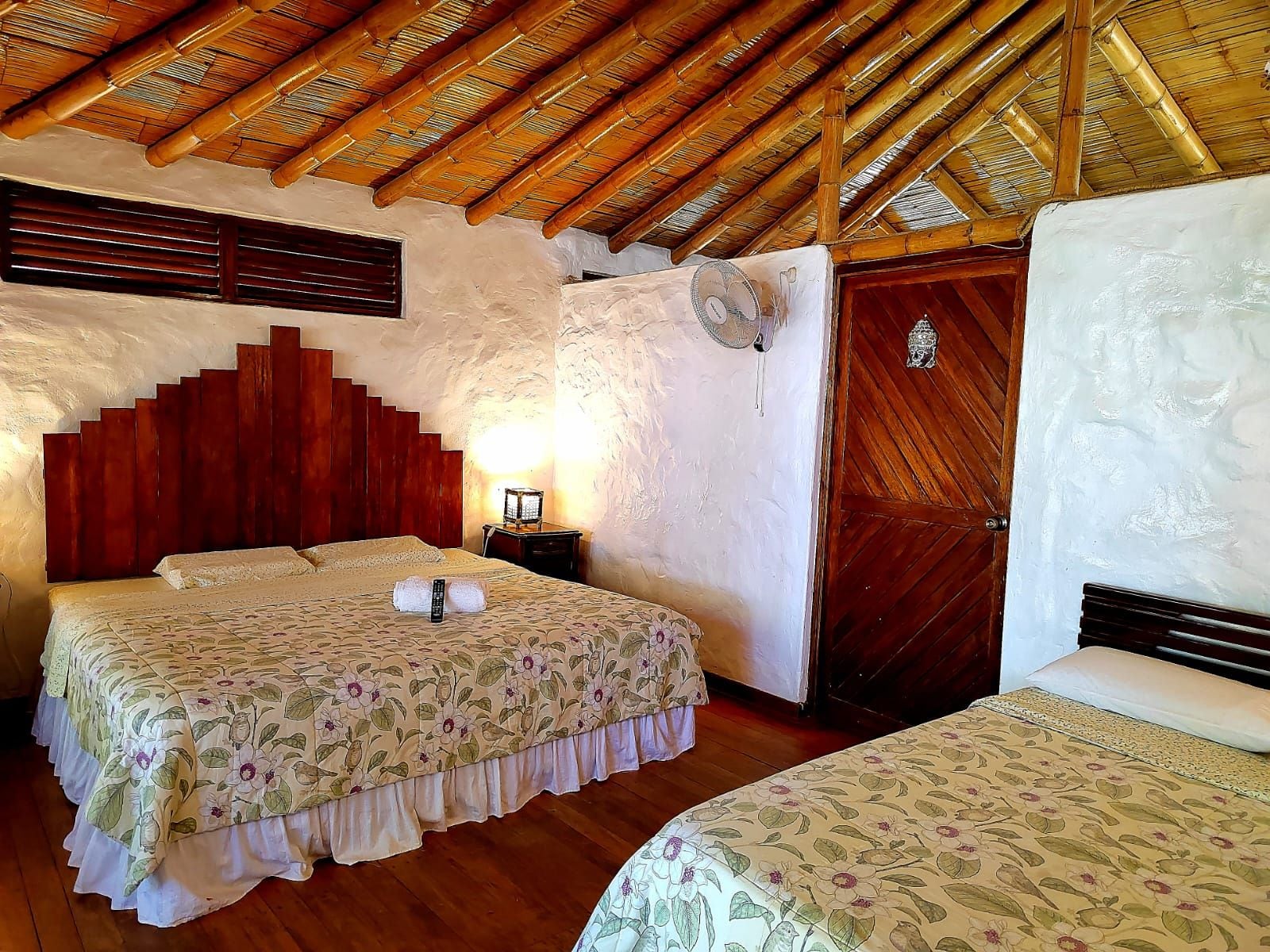 A room with a bed, a nightstand, a wall-mounted fan, and a wooden door.