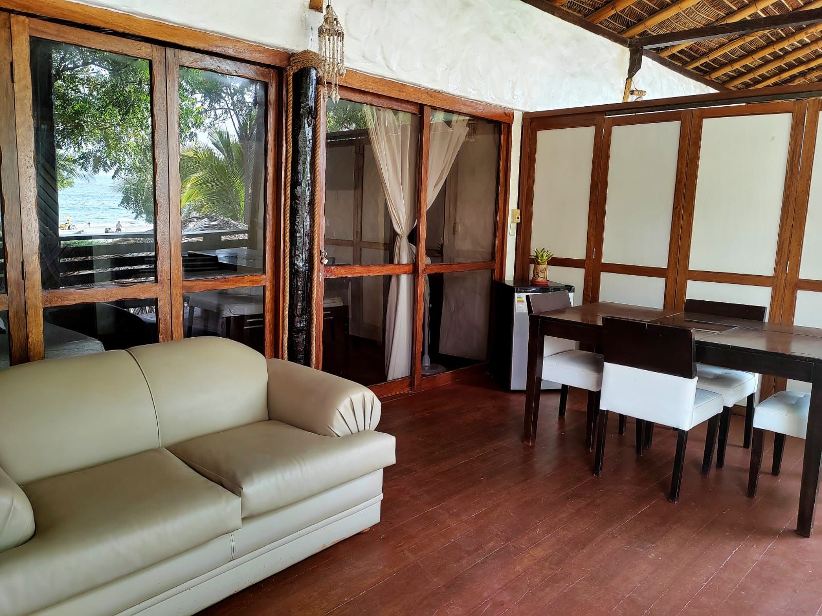 A room with a sofa, a dining table with chairs, and a view of the sea through large windows.