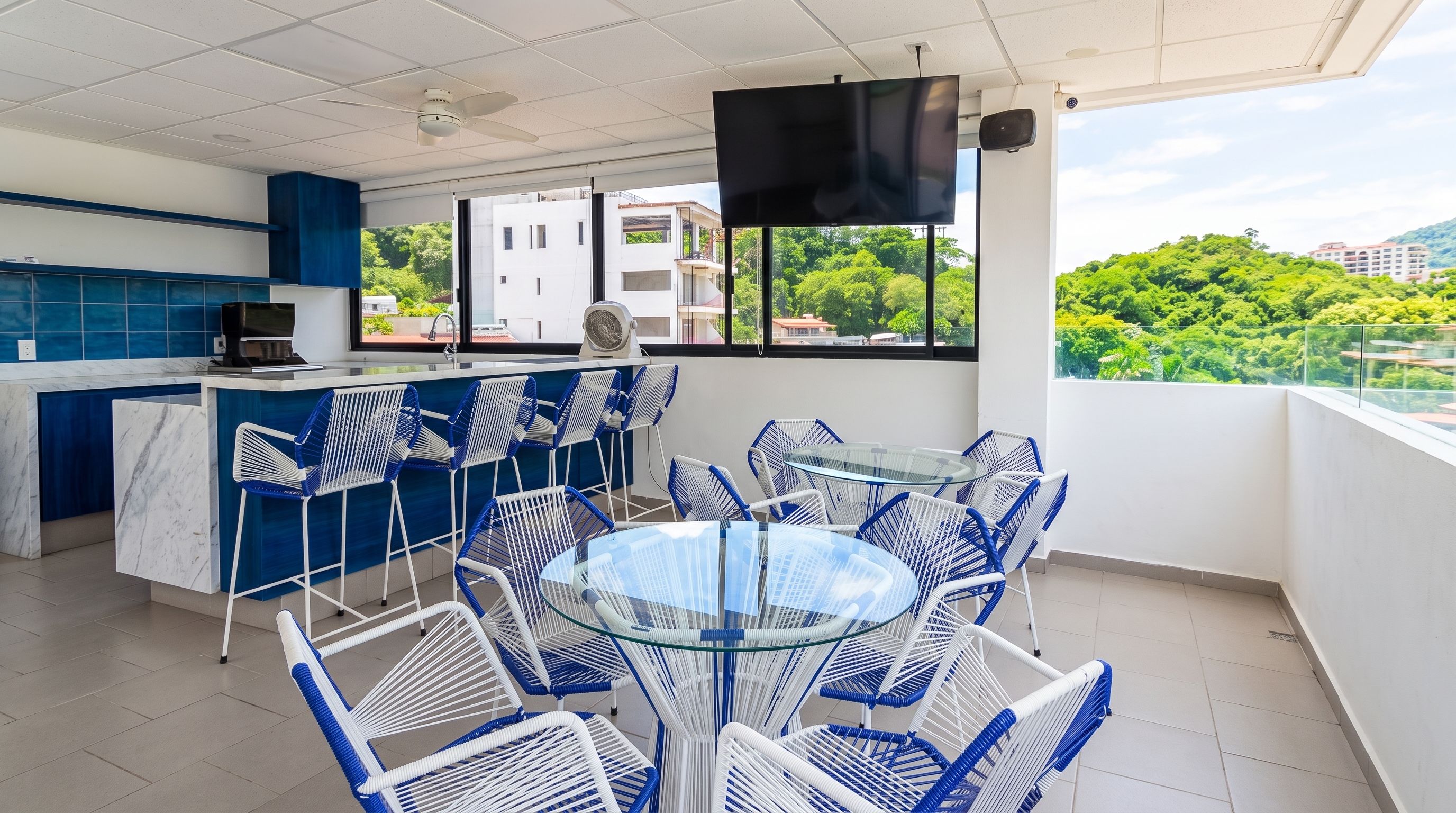 Een moderne keuken met een blauw aanrecht, een bar met blauwe stoelen en een groot raam met uitzicht op groen en gebouwen.