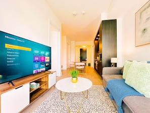 A modern living room with a flat-screen TV displaying a streaming service interface, a round coffee table with a plant, a grey sofa, and a patterned rug. - Modern Downtown Toronto Retreat on Front Street (Toronto)