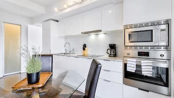 A modern kitchen with a glass dining table, stainless steel appliances, and a potted plant.