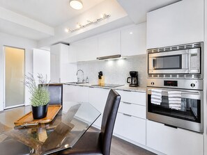 A modern kitchen with a glass dining table, stainless steel appliances, and a potted plant. - StayToronto - The Britt Suites (Toronto)