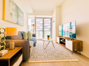 A modern living room with a sofa, a coffee table, a TV, and a large window. - Modern Downtown Toronto Retreat on Front Street (Toronto)