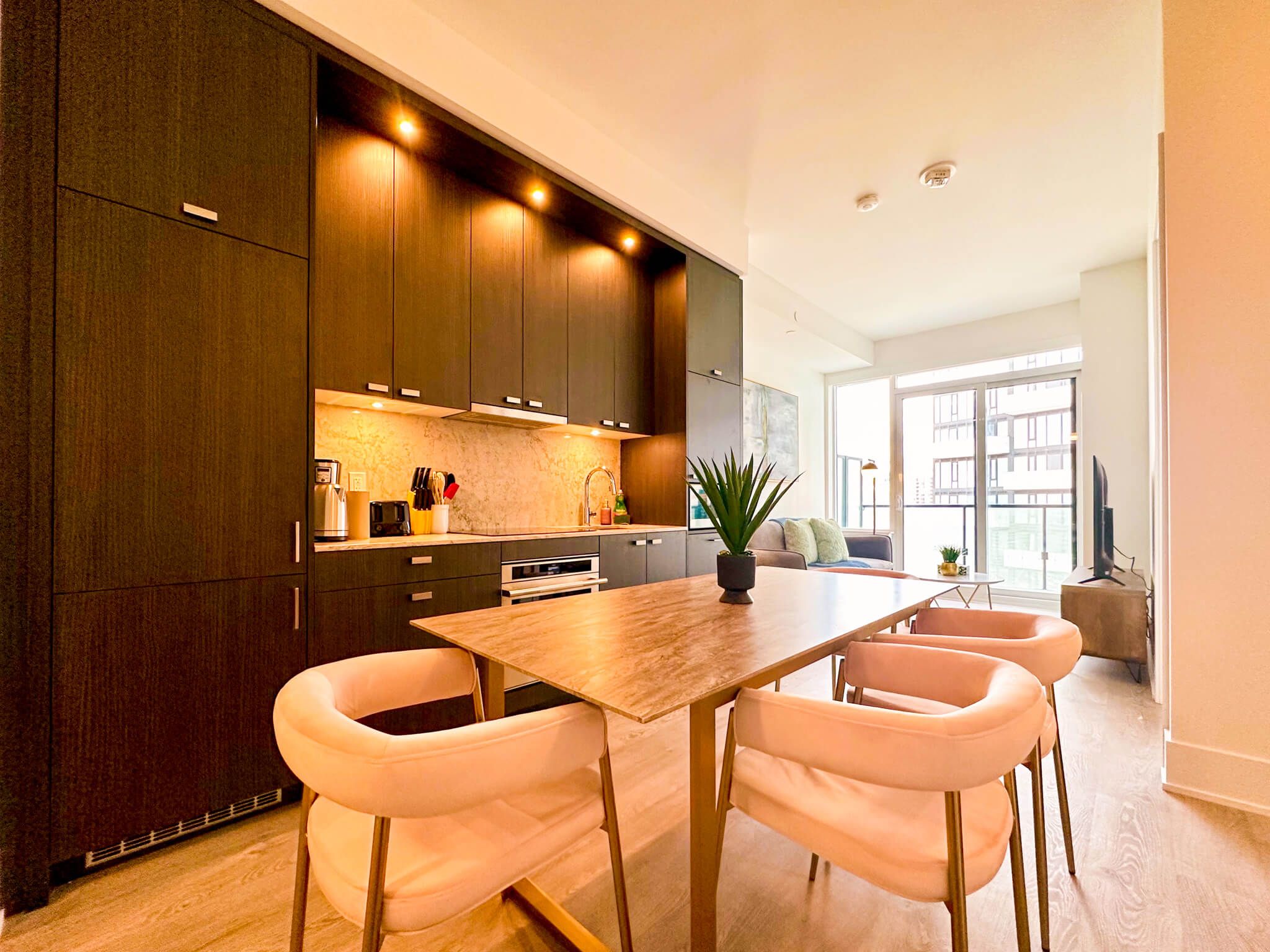 A modern kitchen with dark wood cabinets, a central island, and a dining area with white chairs.