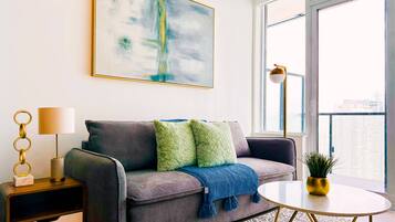 A modern living room with a grey sofa, a blue throw blanket, a gold lamp, and a large abstract painting on the wall.