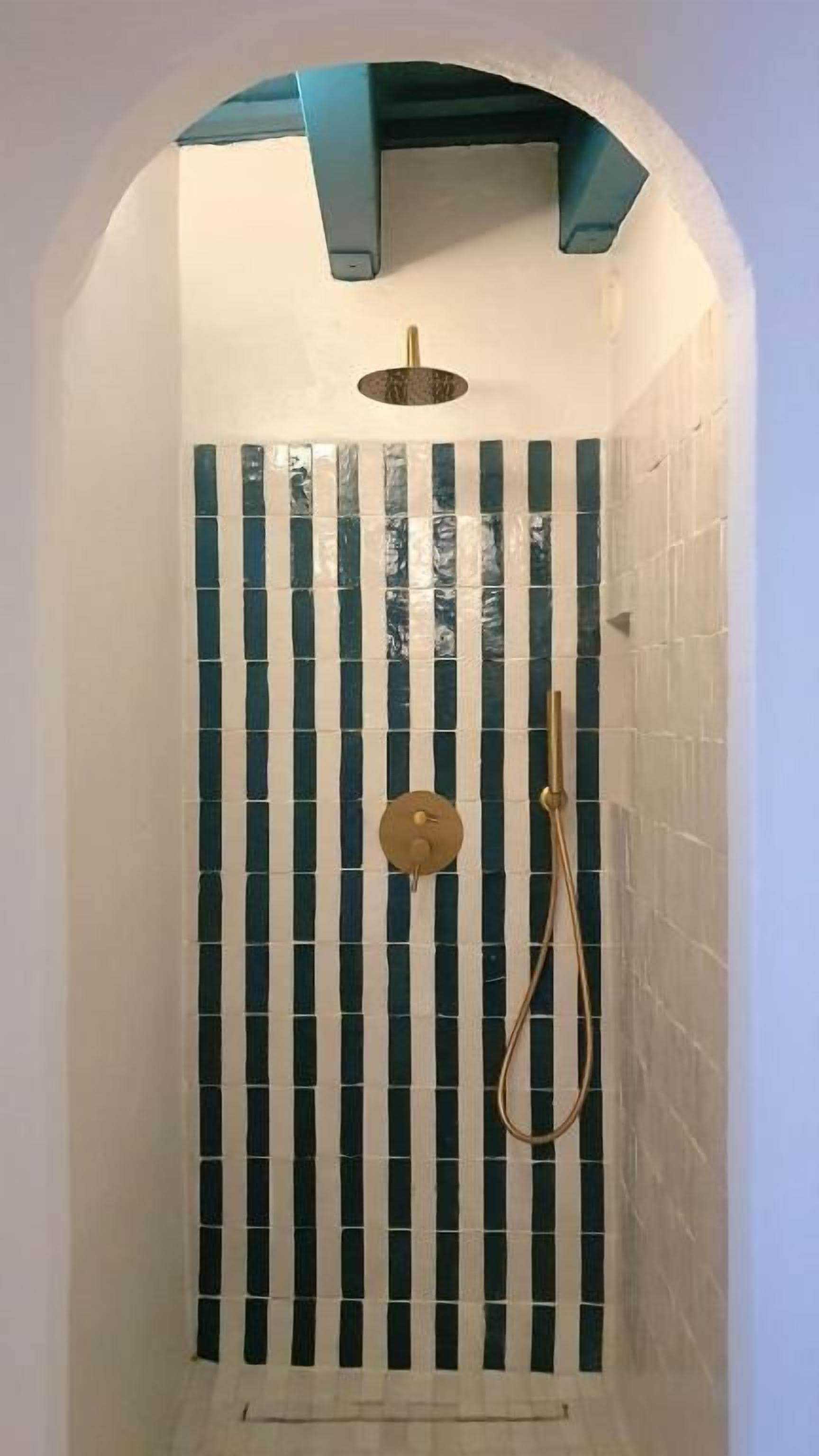 Una ducha con un patrón de azulejos a rayas verticales y un cabezal de ducha de mano.