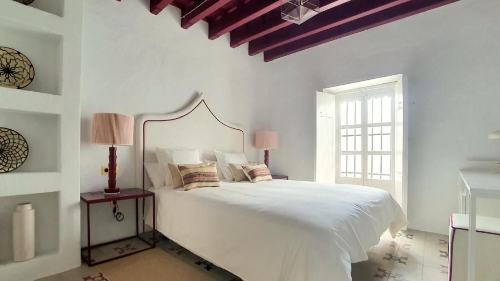 Un dormitorio con cama, lámparas de noche, una ventana y una pared decorada con placas.