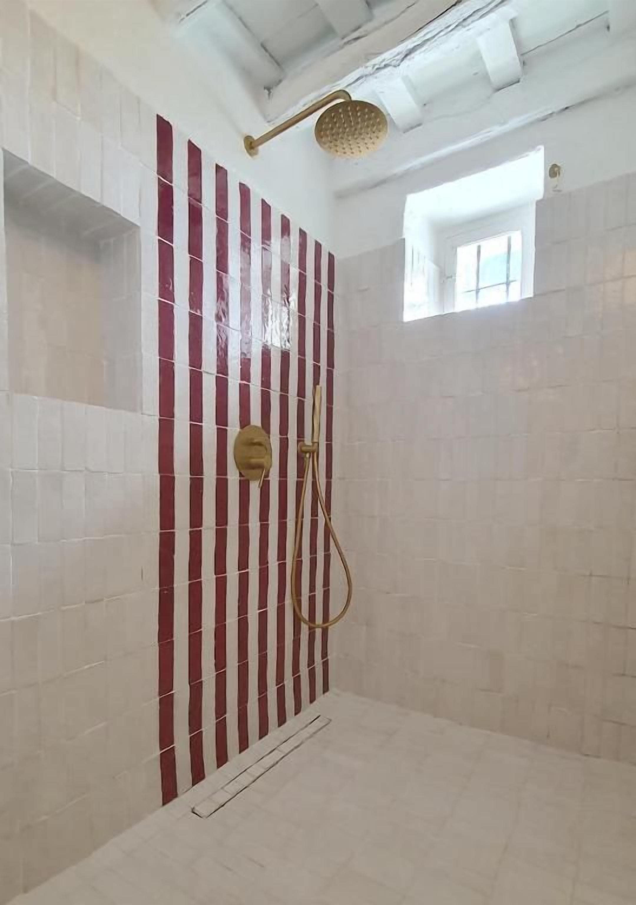 Ducha con cabezal dorado y una ventana encima.