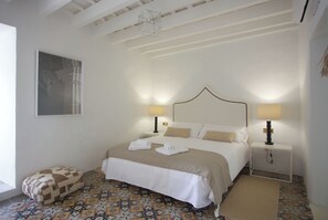 A bedroom with a bed, two bedside tables, a nightstand, a patterned rug, and a framed picture on the wall.