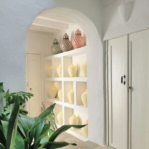 A hallway with a white door, a white shelf with various vases, and a large plant. - Canalejas 3 Vejer (Vejer de la Frontera)