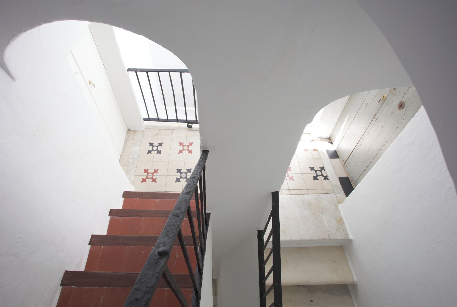 Eine Treppe mit Metallgeländer, weißen Wänden und gefliestem Boden mit Muster.