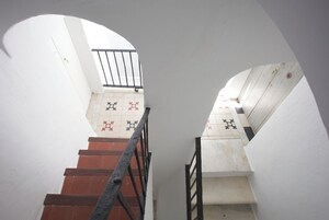 Una escalera con barandilla metálica, paredes blancas y baldosas de suelo con diseño.