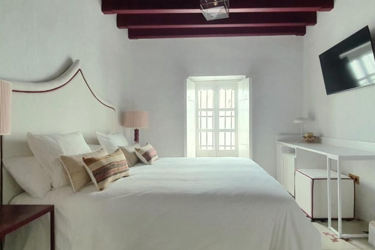 A bedroom with a bed, bedside table, desk, and TV.