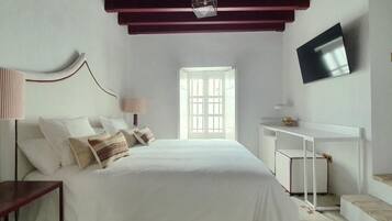 A bedroom with a bed, bedside table, desk, and TV.