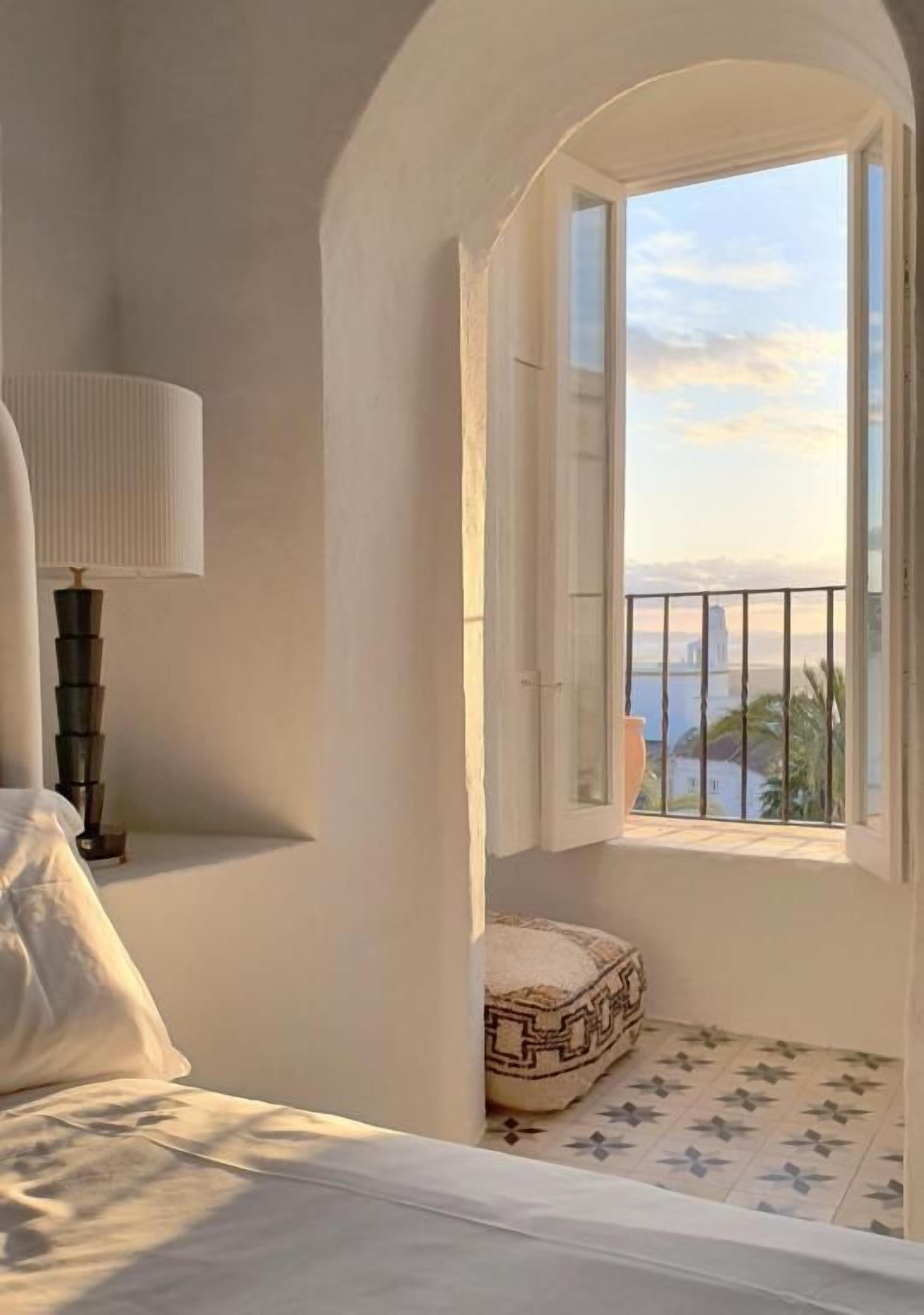 Un dormitorio con cama, lámpara de noche, ventana con vistas y suelo estampado.