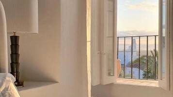 Un dormitorio con cama, lámpara de noche, ventana con vistas y suelo estampado.