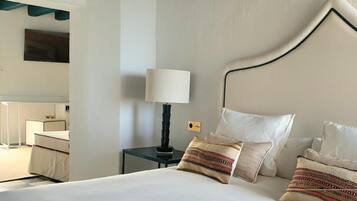 Habitación de hotel con cama, mesita de noche con lámpara, espejo y televisor montado en la pared.