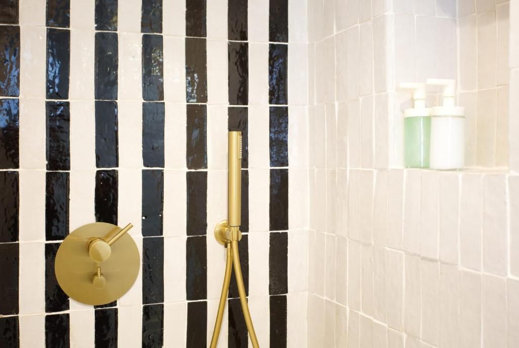Ein Badezimmer mit schwarz-weiß gefliesten Wänden, einem goldfarbenen Duschkopf und einer Shampoo-Flasche.