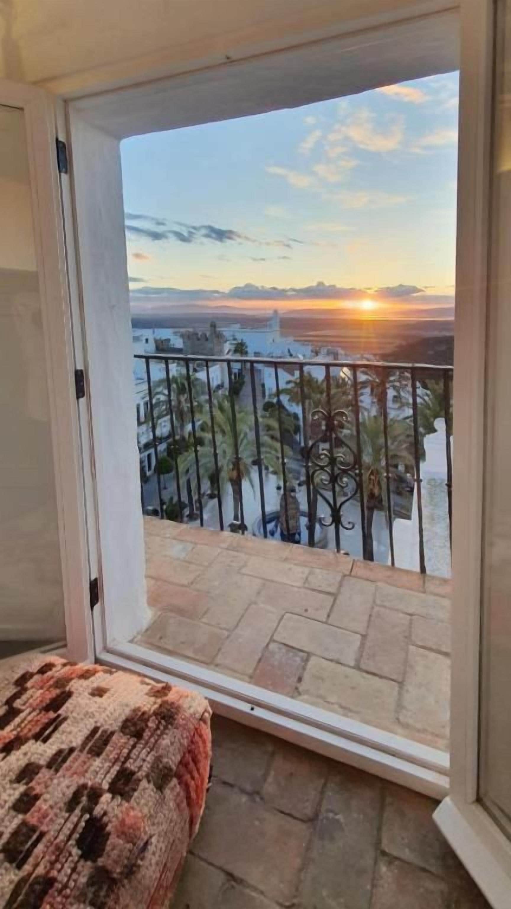 Ein Balkon mit Blick auf einen Sonnenuntergang über dem Wasser, einem Geländer und einem gemusterten Teppich.