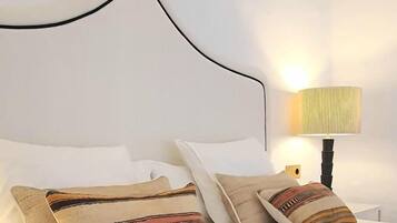A bed with white pillows and a patterned throw, a bedside lamp, and a plain wall.