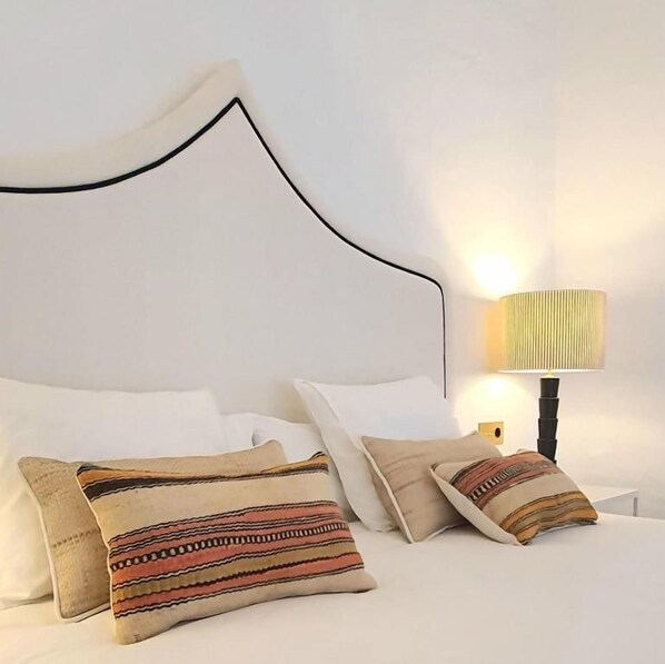 Una cama con almohadas blancas y una colcha estampada, una lámpara de noche y una pared lisa.