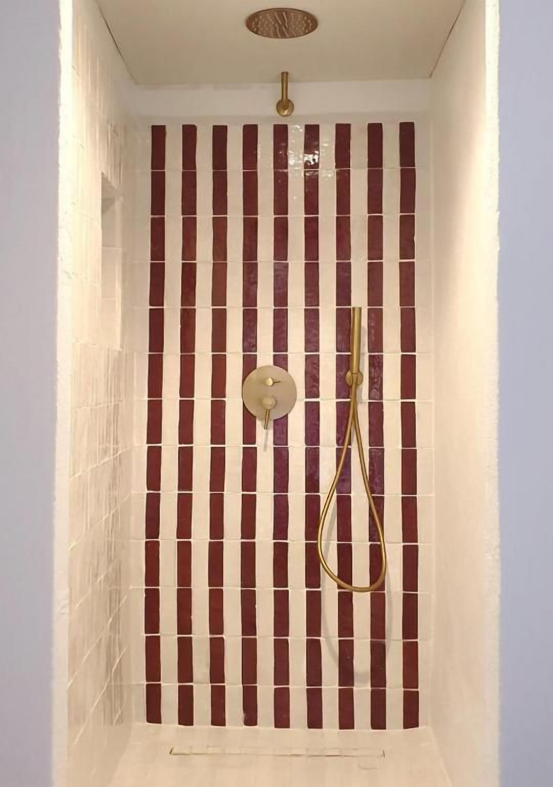 Eine Dusche mit Wandfliesen in vertikaler Streifenoptik, einer Handbrause und einer an der Wand befestigten Armatur.