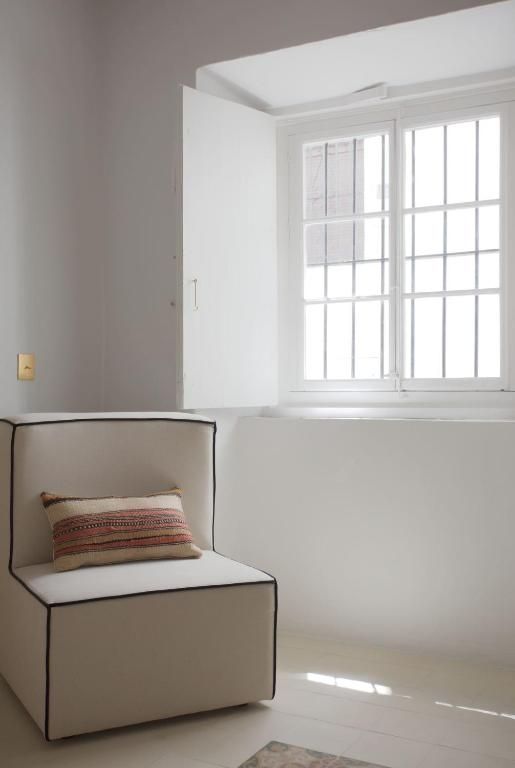 Una habitación con una silla blanca, una ventana de marcos blancos e interruptor de luz en la pared.