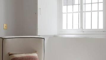 Una habitación con una silla blanca, una ventana de marcos blancos e interruptor de luz en la pared.